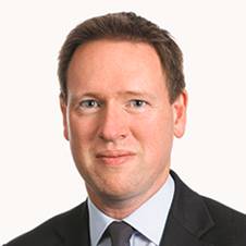 A person wearing a suit and tie smiling at the camera
Description automatically generated