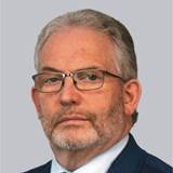 A person wearing glasses and a suit
Description automatically generated